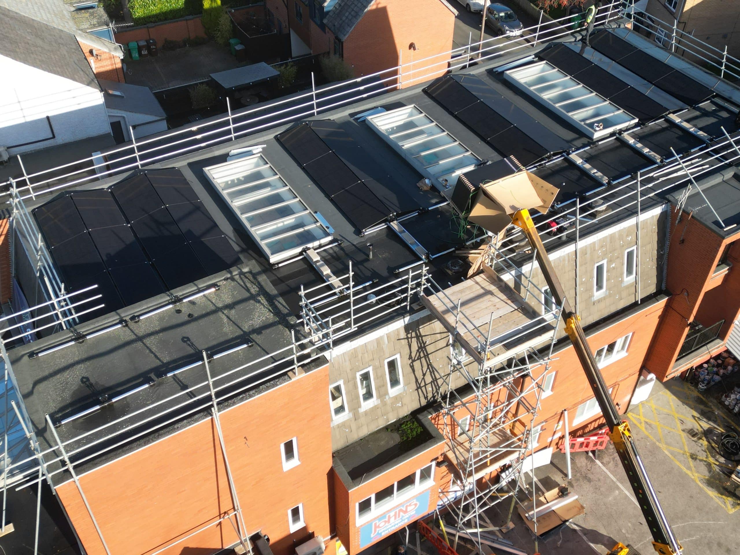 Commercial solar installation in progress showing scaffolding and telehandler lift at Johns of Nottingham three-storey building