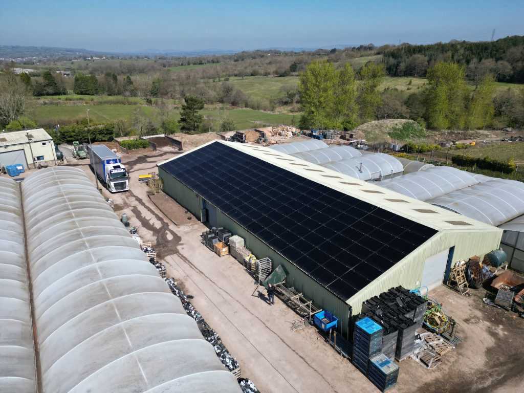 Long farm nursery barn with its whole roof covered in all-black solar panels, polytunnels alongside, installed by Spectrum Energy Systems