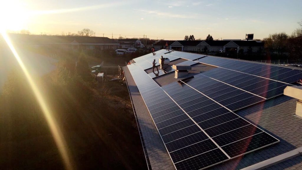 Installers fitting solar panels on a school roof at sunrise